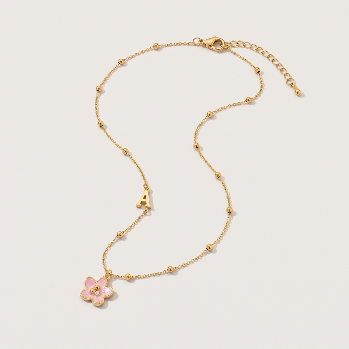 Amelie Initial Necklace - ARWELY, gold ball chain with the letter A and a pink enamel flower, full view on a grey studio background