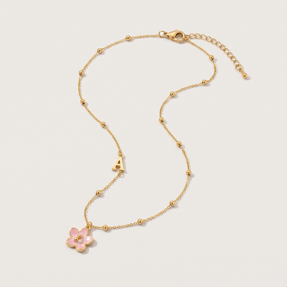 Amelie Initial Necklace - ARWELY, gold ball chain with the letter A and a pink enamel flower, full view on a grey studio background