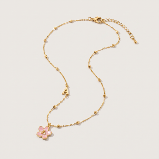 Amelie Initial Necklace - ARWELY, gold ball chain with the letter A and a pink enamel flower, full view on a grey studio background