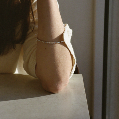 Rivière Tennis Bracelet worn on the wrist, resting on a cafe table in afternoon light